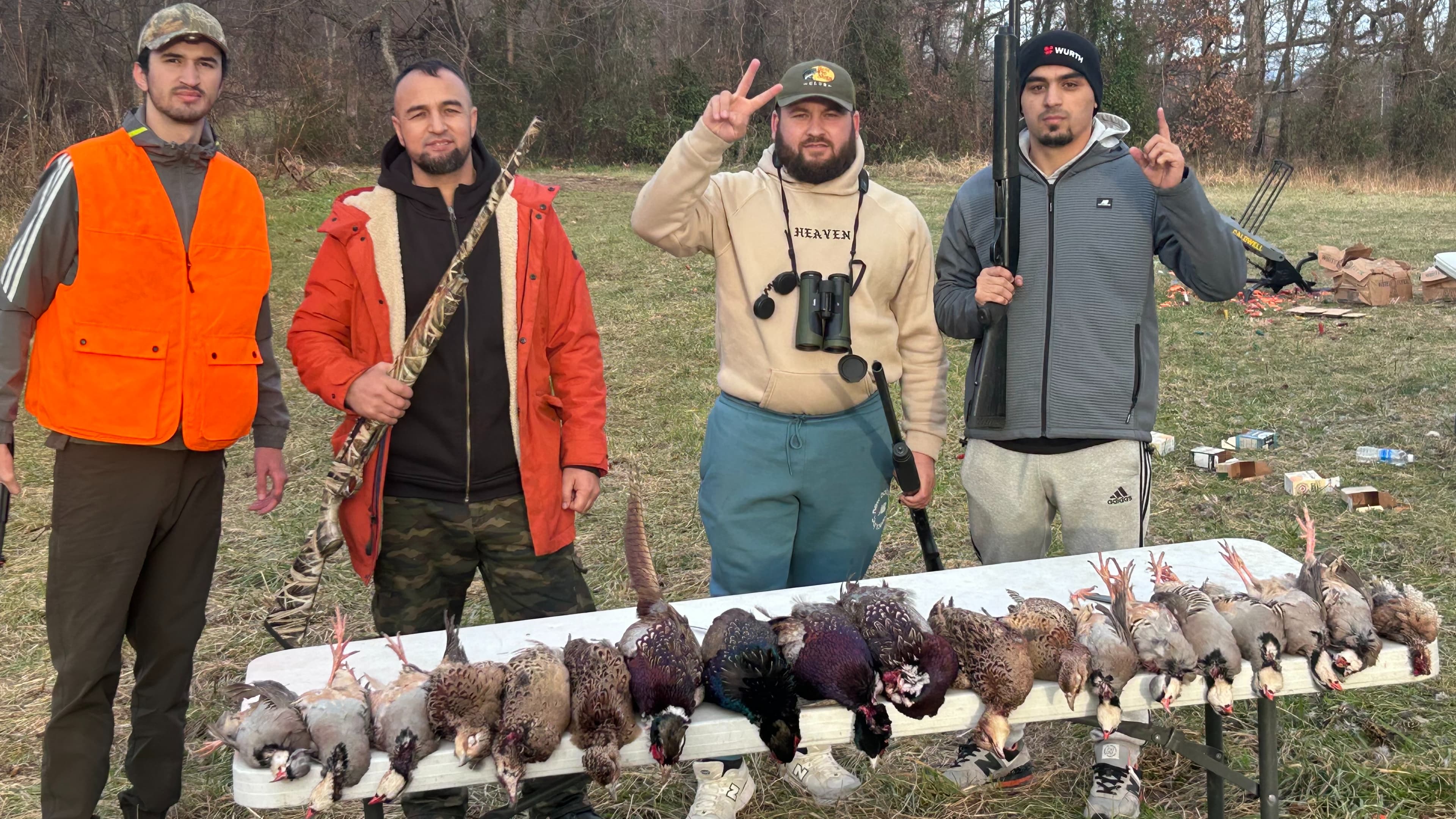 Four hunters pose with a table full of harvested birds, including pheasants and quail, outdoors.