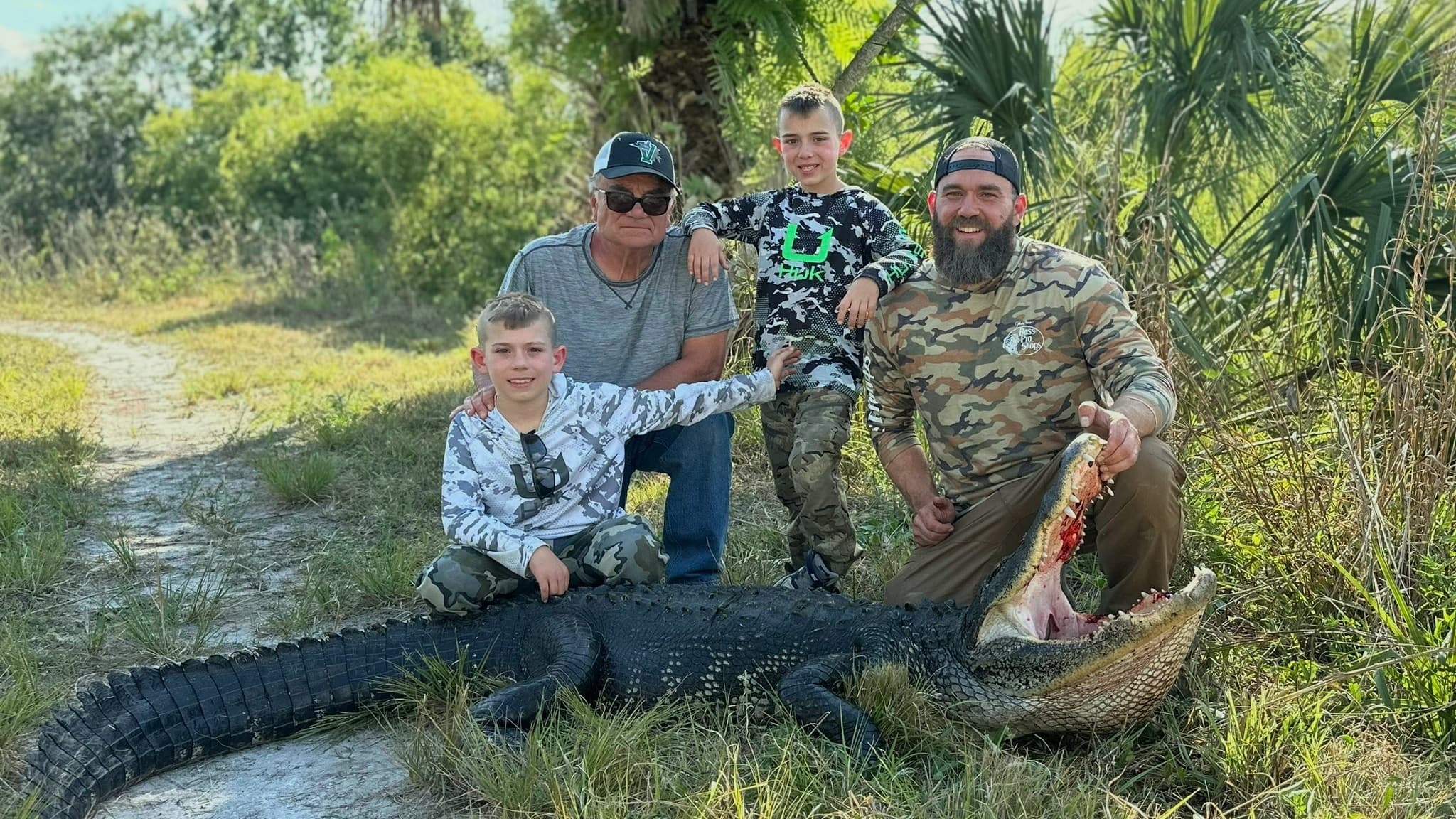 Four people pose with a large alligator.