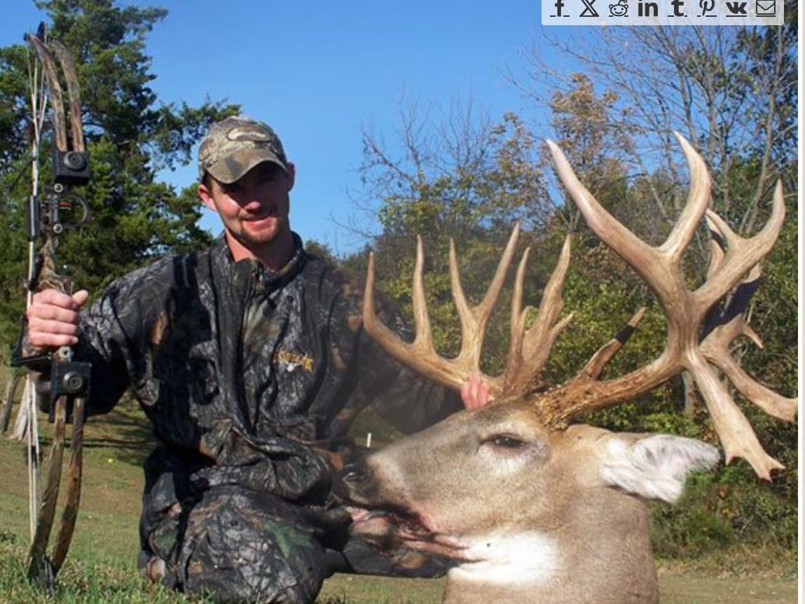 Hunter in camouflage holds bow beside large buck with impressive antlers.