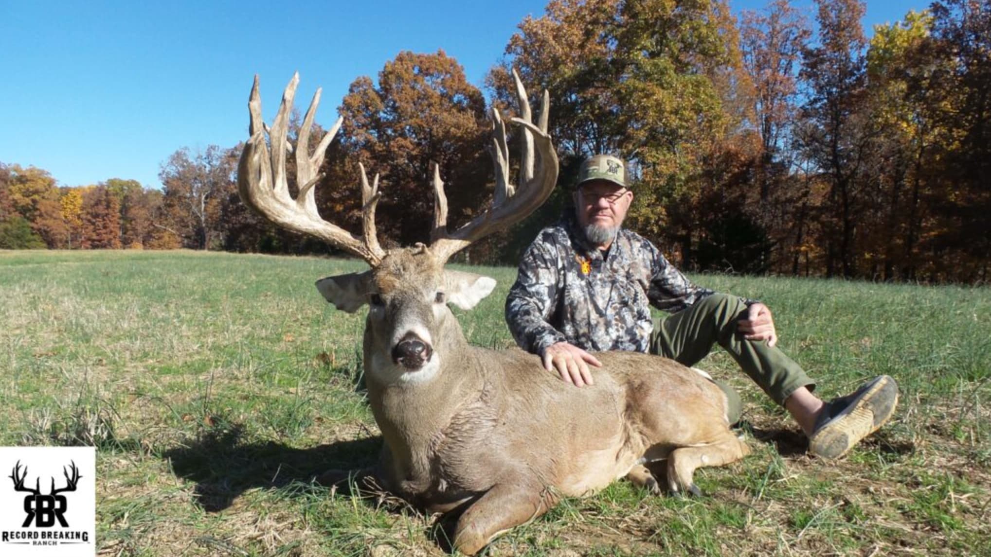 Hunter posing with a large whitetail buck in a grassy field.